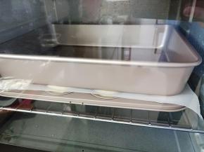 贝壳模具里的面团发酵至1.5倍大后盖上一张油纸上面压一个烤盘，送入预热好的烤箱，同样150度烤20分钟