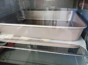 贝壳模具里的面团发酵至1.5倍大后盖上一张油纸上面压一个烤盘，送入预热好的烤箱，同样150度烤20分钟