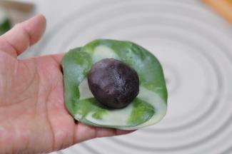 取一个卷，将两头往中间捏合后按压，擀开成圆形，取一份红豆沙馅放入包裹起来，捏紧收口。