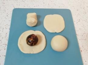 让两头翘起，压扁擀成圆形，放入枣泥核桃馅，用虎口慢慢向上推挤捏紧收口。