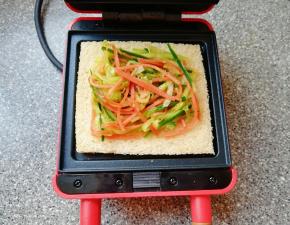 预热好的三明治早餐机下盘放上一片全麦吐司，放上炒好的蔬菜。
