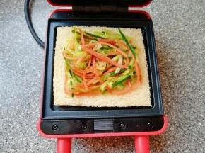 预热好的三明治早餐机下盘放上一片全麦吐司，放上炒好的蔬菜。