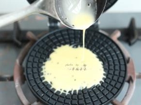 用勺子舀一勺面糊倒入蛋卷模具中间位置，面糊会自动朝旁边溢开，溢开至模具3/4圆周满时，立即合上蛋卷模，放在燃气灶上小火加热1分钟，然后翻过来模具反面加热40秒左右，直至蛋卷呈微黄色