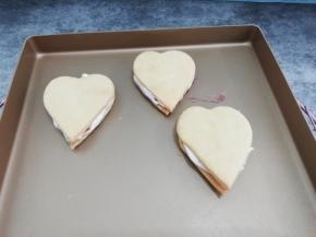 然后把另一个盖在棉花糖上，在剪一个小一点的心形，放在心形饼干上，筛上可可粉即可