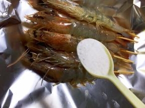 插好竹签的大虾放在锡纸上，撒盐
