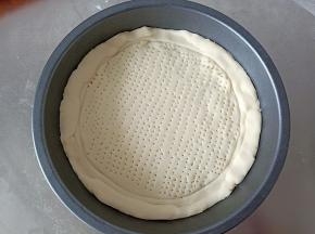 将面团擀成和披萨盘一般大小的圆，放入披萨盘，压出边边来，用叉子在饼底戳一些孔洞