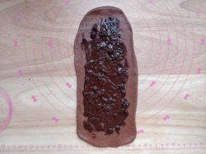 取一块面团，擀成长条状的薄片，将巧克力酱和蔓越莓干涂在上面。