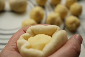 取第一个滚圆的面剂子，按扁或者擀开都可以，再加入一个奶黄馅，用虎口法慢慢推上去，最后收口捏紧。