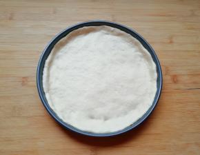 发酵好的面团揉光排气，擀成一张比模具大一些的面饼，放进披萨盘里，用手把大出来的部分压实，使其贴在披萨盘的边上。