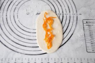 取一个醒好的面团擀成长㮋形，放入提前煮好的糖渍橙皮。