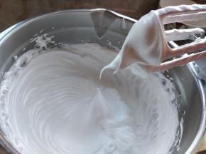 继续一边打发蛋白，一边把煮好的糖浆慢慢以细线状倒入蛋白中，持续打发到室温。这时蛋白糖霜越来越有光泽且坚挺。