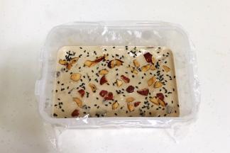 把拌好的糯米糊倒入盒中，用手动打蛋器搅拌下，接着撒上红枣碎和黑芝麻。
