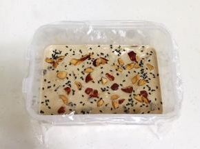 把拌好的糯米糊倒入盒中，用手动打蛋器搅拌下，接着撒上红枣碎和黑芝麻。