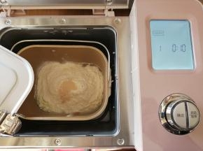 依次放入水、蛋液、糖、盐、奶粉和面包粉，在面粉顶端加入酵母，将面包桶放入到东菱JD08面包机里，选择和面程序10分钟