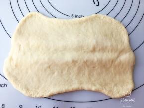 醒好面团擀成两边薄中间厚一些的长方形，用擀面杖在中间压一下。