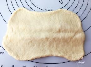 醒好面团擀成两边薄中间厚一些的长方形，用擀面杖在中间压一下。