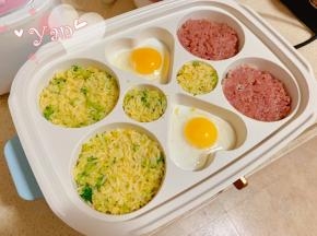 将爱心盘刷上少许油，将电热锅调至中档加热半分钟，装入米饭压平，打入鸡蛋，放入猪绞肉压平。