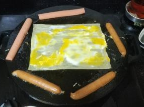 将鸡蛋平均摊开，切开的香肠放边上加热