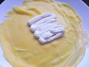 9.	取一张饼皮，挤上适量的淡奶油，摆上芒果肉，再挤上一层淡奶油，然后将其包好，芒果班戟就做好了，冷冻后品尝味道更佳。