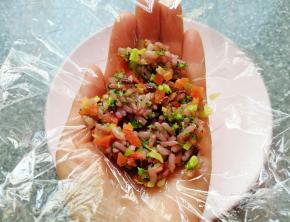 手掌心里放上一张保鲜膜，舀入拌好的杂粮蔬菜饭，提起保鲜膜的四个角，用手捏好饭团。