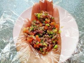 手掌心里放上一张保鲜膜，舀入拌好的杂粮蔬菜饭，提起保鲜膜的四个角，用手捏好饭团。