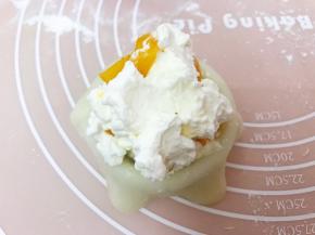 取一份面皮用手轻轻拉扯的更为薄一些放入雪媚娘模具里，舀入一大勺淡奶油再放入芒果粒，最后上面再盖上一勺淡奶油