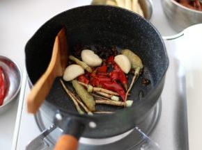 所有的菜都处理好后，重新在锅内倒入少许花生油，将花椒、大料、姜、蒜瓣、剁椒碎、泡山椒、香菜根煸香。
