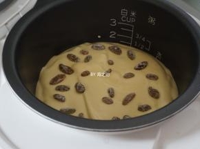 蛋糕糊倒入电饭锅内胆，在桌面上震两下，震出气泡，然后在上面铺上剩余的葡萄干装饰，盖上盖子，选择蛋糕功能键，默认40分钟