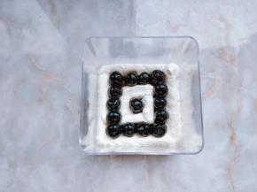 20. 先将少许黑糖液刷在底部的蛋糕片上，再将奶茶奶油如图呈“回字形”挤在盒子中，中间用小勺摆好黑糖珍珠。（珍珠上的黑糖汁不必完全沥净）