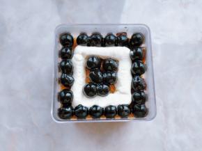 21. 表面放一层蛋糕片压实，刷一层黑糖液，再把四周摆好一圈黑糖珍珠，在中间挤上奶茶奶油。