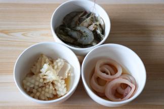 明虾剪掉虾枪、挑出虾线和头部的内脏，跟鱿鱼花、鱿鱼圈一起清洗干净后加入适量生抽、料酒、盐腌制20分钟左右；