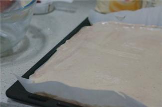 烤盘里铺上一纸烘焙纸，将拌好的面糊倒在里面，刮至平整。入烤箱180度烤制12分钟。