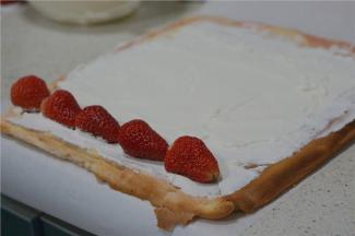 将烤好的蛋糕片取出放凉脱纸，然后打上一份淡奶油抹码在蛋糕片上，再用草莓点缀一下由下至上卷好。
