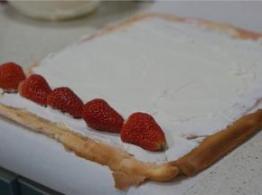 将烤好的蛋糕片取出放凉脱纸，然后打上一份淡奶油抹码在蛋糕片上，再用草莓点缀一下由下至上卷好。