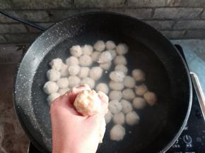 用左手抓取适量的鱼肉泥，从虎口位置挤出，用勺子把鱼丸刮到热水里