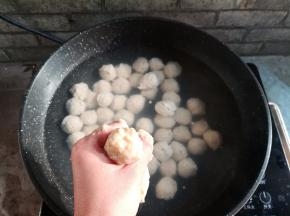 用左手抓取适量的鱼肉泥，从虎口位置挤出，用勺子把鱼丸刮到热水里