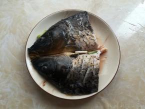 找一个有深度的盘子，先放入适量的姜片和葱白，放入对半切开的鱼头，鱼肉上黑色的内膜要撕掉，鱼头往右部分划2刀，抹上2克盐简单入味，淋上料酒去腥，鱼头的2面都要淋料酒，腌制10分钟左右