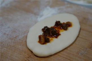 擀面牛舌头状之后，码上适量的牛肉酱及少许的荞头末。然后再卷包好入模具里。