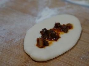 擀面牛舌头状之后，码上适量的牛肉酱及少许的荞头末。然后再卷包好入模具里。