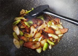 倒入点清水把腊肉煮制沸腾会，先把蒜白部分放入翻炒变软。