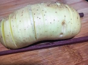 土豆带皮洗净，左右两边夹两根筷子，切片不切断，类似手风琴一般