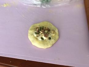 松弛后取一份面团轻拍排气，稍擀扁擀圆后放上适量奶酪馅和果仁碎。