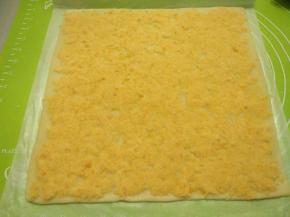 把咸蛋黄肉松均匀平铺在饼皮表面，尾部预留约1厘米，其他三边铺满。盖上油纸，用擀面杖轻擀表面，让咸蛋黄肉松馅和饼皮完全贴合。