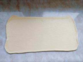 把面团旋转90度，沿接缝的方向把面片擀成0.5cm的厚片（先按压中间接口处来回滚动，然后再整块从头到尾擀动。擀面时要使用走锤，用力均匀，这样黄油夹层才能分布均匀）。