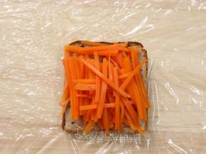 加热好的吐司片放在保鲜膜上面，先铺上胡萝卜，挤上沙拉酱。