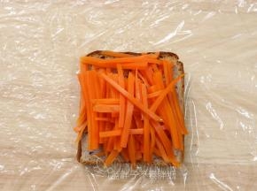 加热好的吐司片放在保鲜膜上面，先铺上胡萝卜，挤上沙拉酱。