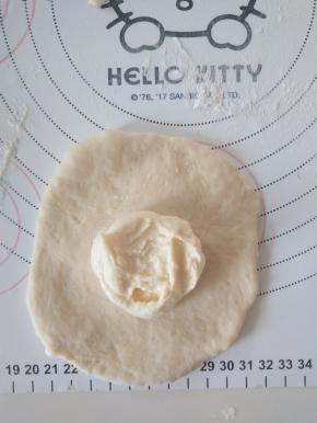 取一个面团，擀成圆形，翻面，包入适量奶酪馅。收紧封口。