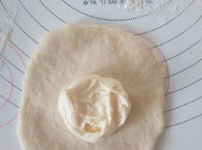 取一个面团，擀成圆形，翻面，包入适量奶酪馅。收紧封口。