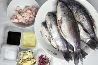 准备食材，鲫鱼去鳞去内脏洗净，猪肉切丁，葱姜蒜切开。