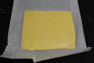 将原味面团放在一张长油纸的一侧，多余的油纸盖在面团上，用擀面杖擀成薄的长方形片。